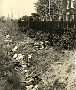 602860 Afbeelding van gedumpt afval in de spoorsloot achter de schutting langs de Cremerstraat te Utrecht.